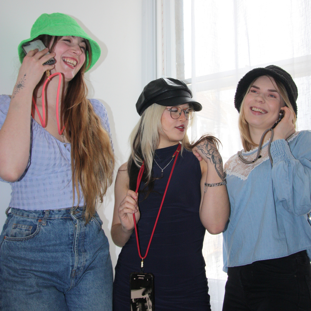 Three girls posing and smiling. Wearing different coloured crossbody phone strap ropes each.